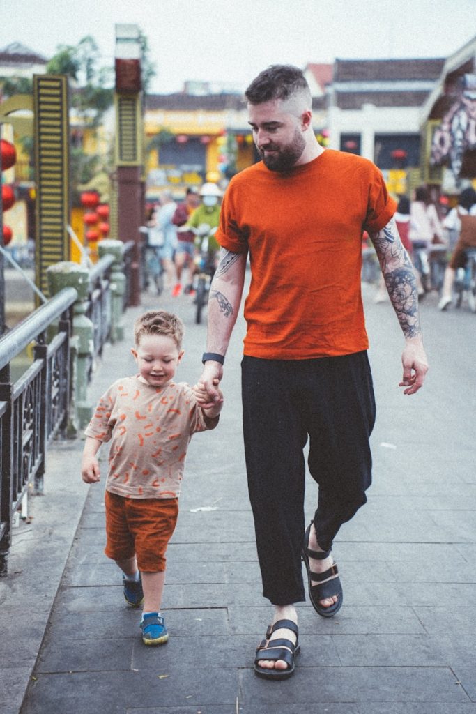 a man walking down a sidewalk holding the hand of a small child